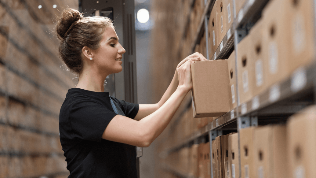 Young woman with bun in warehouse pulling box from shelf