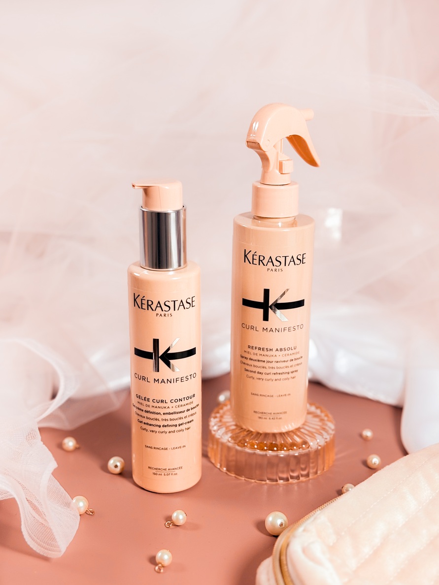 Les soins Kérastase Curl Manifesto, dont la gelée définissante et le spray rafraîchissant, posés sur un fond délicat avec voile en tulle et perles.