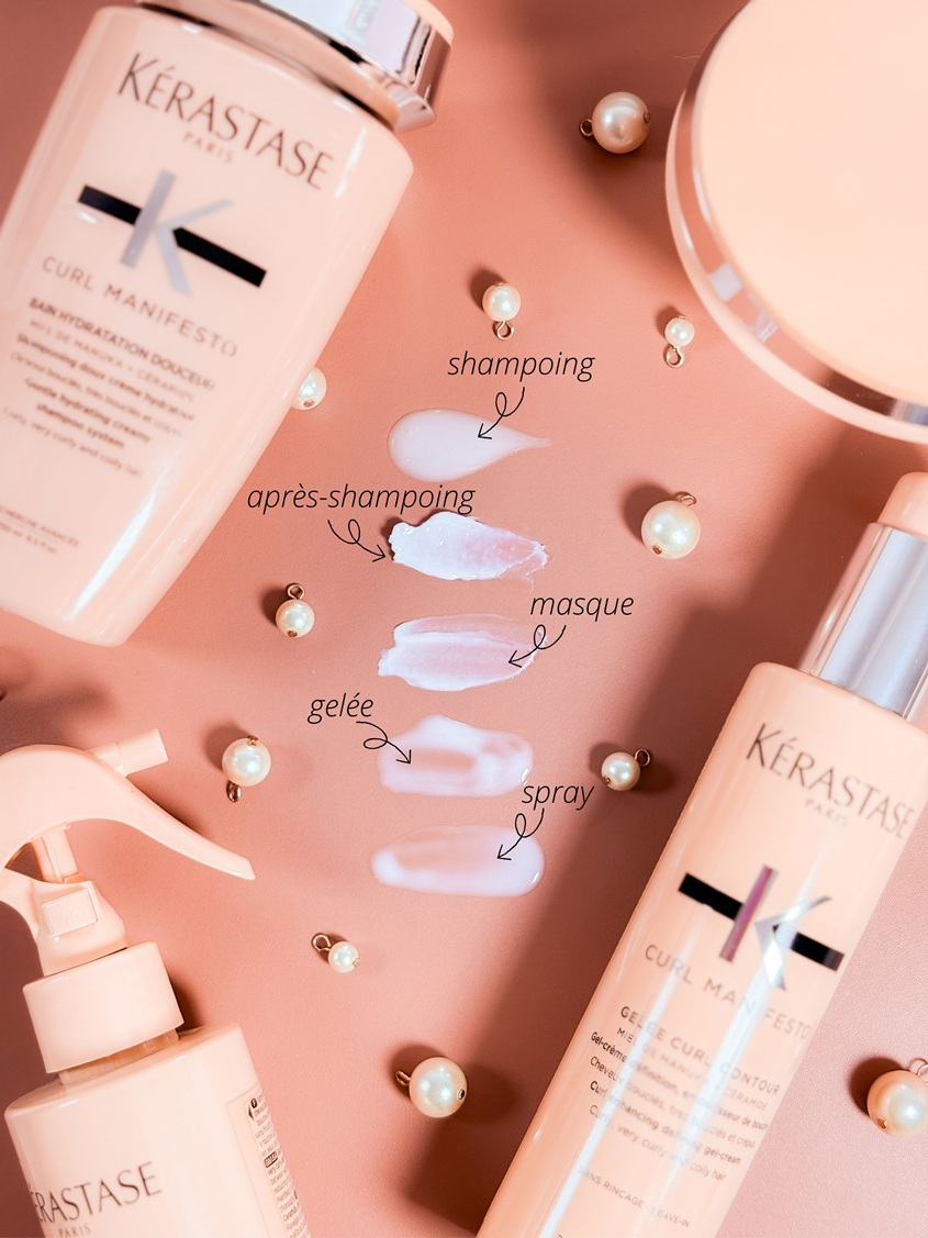 La gamme Kérastase Curl Manifesto avec ses textures de shampoing, après-shampoing, masque, gelée et spray présentées sur un fond rose délicat avec perles et flacons de la routine en arrière-plan.