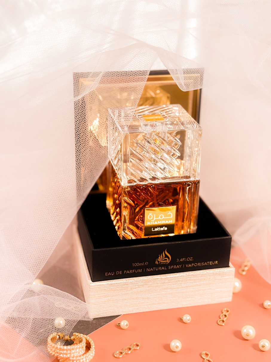 Le parfum Lattafa Khamrah dans son flacon ambré facetté, posé dans sa boîte ouverte sur un fond élégant avec voile en tulle, perles et bijoux dorés.