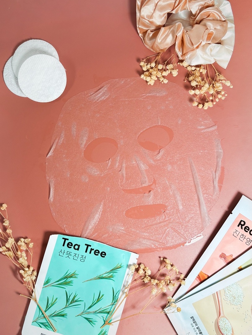 Le masque en tissu Missha Airy Fit Mask déplié sur un fond rose délicat avec cotons, fleurs séchées et chouchous satinés.