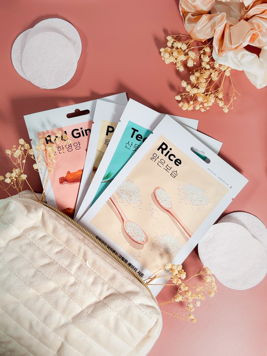 Les masques en tissu Missha Airy Fit Mask rangés dans une trousse ouverte, sur un fond rose délicat avec cotons, fleurs séchées et chouchous satinés.