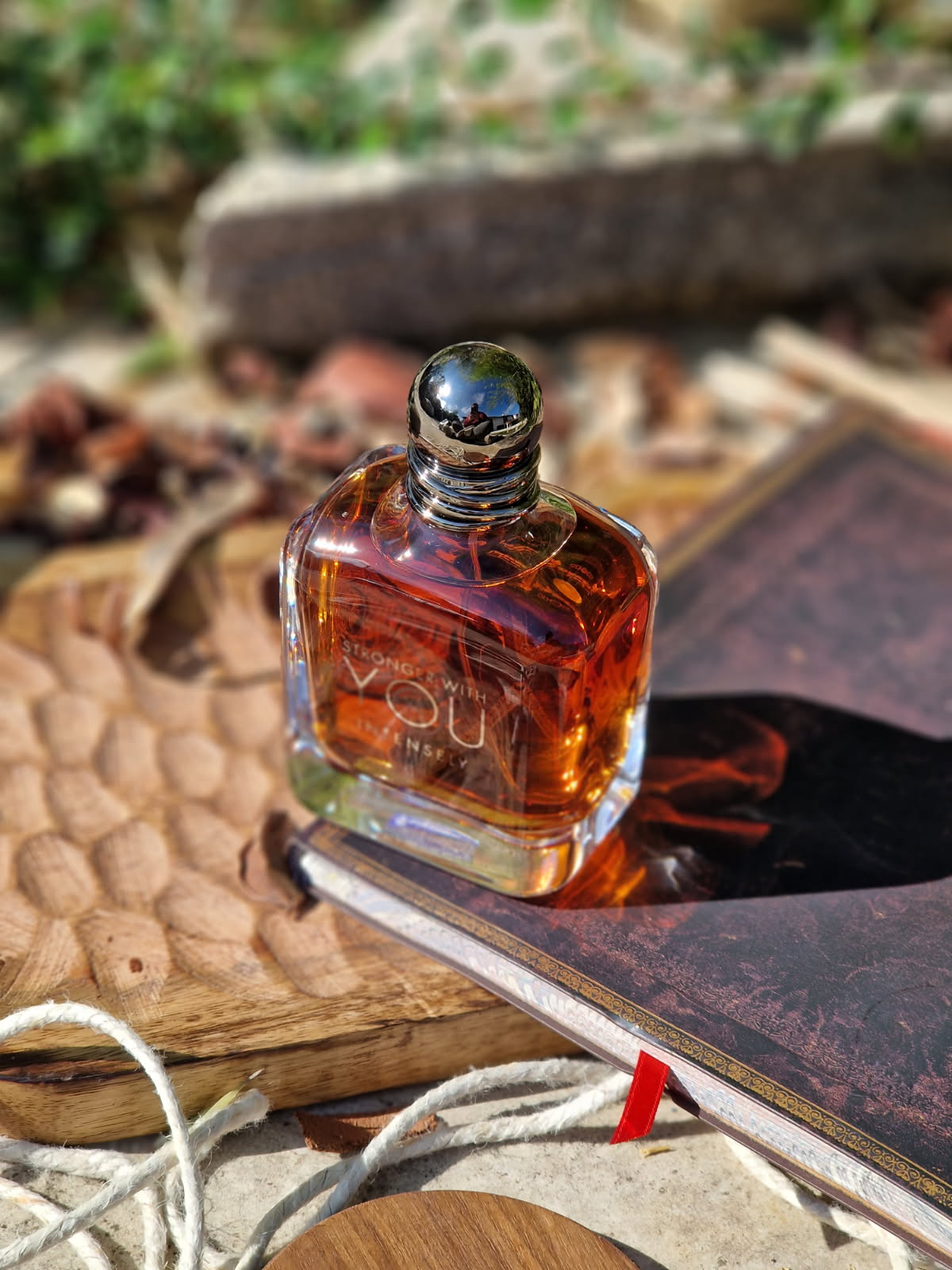 Le parfum Emporio Armani Stronger With You Intensely posé seul, dans son flacon ambré aux reflets chauds, sur une planche en bois avec carnet, corde et épices en arrière-plan, dans une mise en scène élégante aux accents masculins et raffinés.