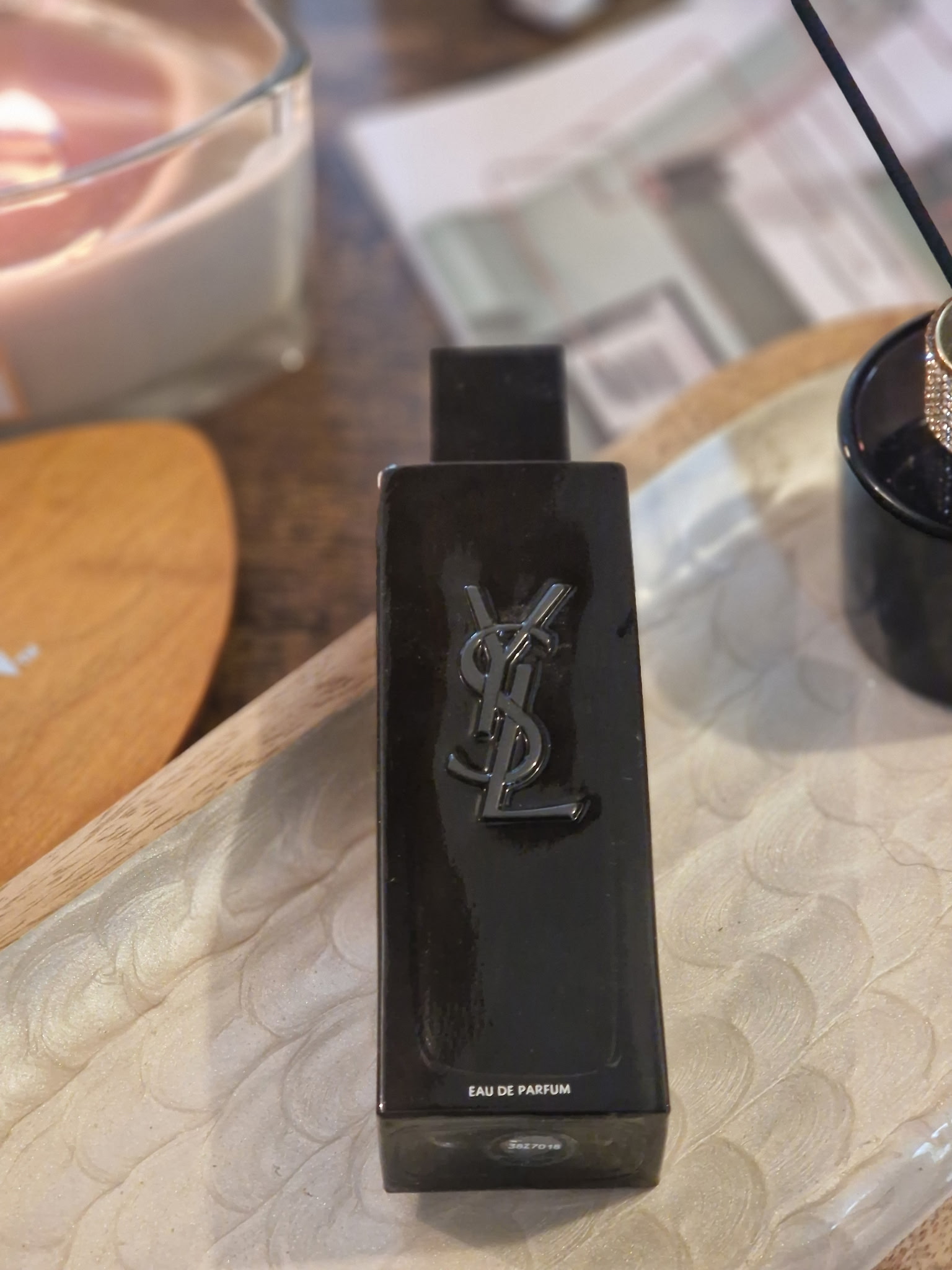 Le parfum Yves Saint Laurent MYSLF ouvert, avec son flacon noir laqué sans capuchon, posé sur un plateau aux côtés d’une bougie allumée, d’un diffuseur et d’un magazine, dans une ambiance chaleureuse et cocooning.